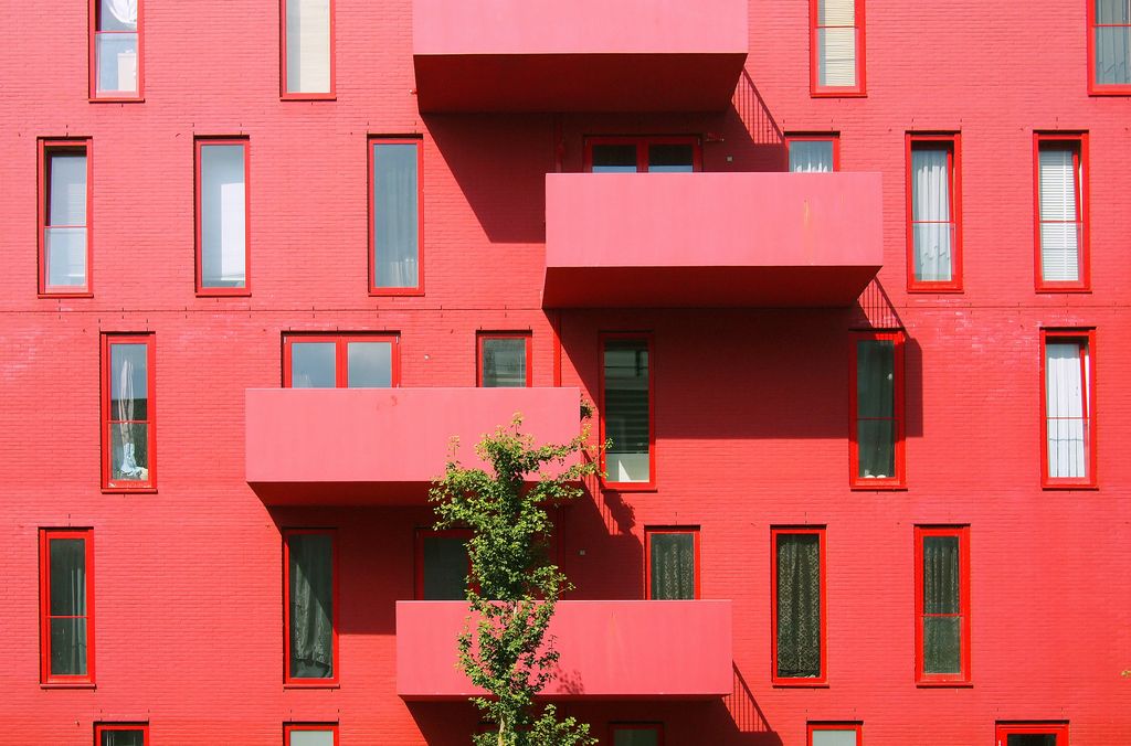 A vibrant red apartment building with asymmetrical balconies, illustrating the concept of 3D apartment rendering for architectural design.